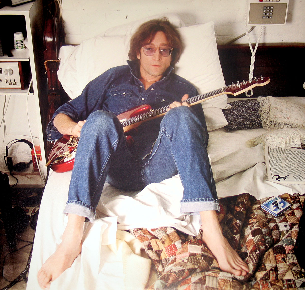 Photo of John Lennon sitting on the bed playing a Fender Stratocaster guitar look-a-like
